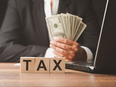 Close-up of wooden cubes with letters TAX with a businessman holding US dollars banknote blurred background photo