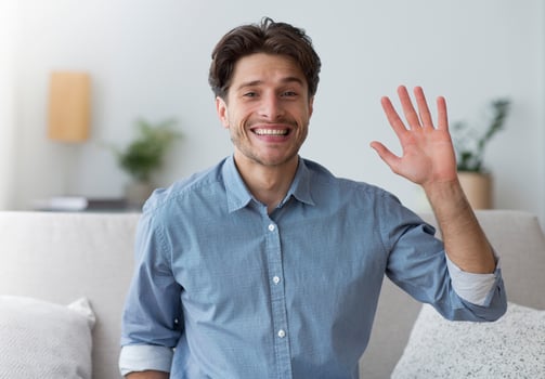 Hello. Smiling Man Waving Hand Looking At Camera Sitting On Sofa Indoor. photo