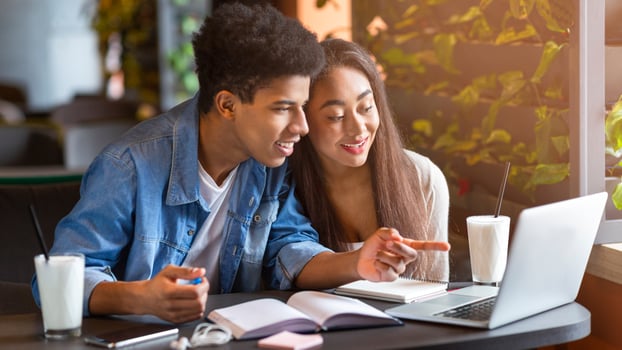 A young loving black couple sits at a table in a bustling cafe, focused on the screen of a laptop. They appear engaged in conversation as they review information on the device. photo