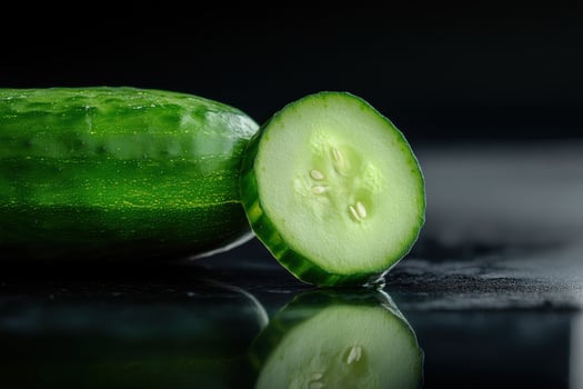 Freshly sliced cucumber with green skin and seeds placed on a reflective black surface photo