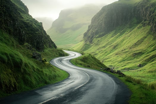 Winding road through lush green hills of a misty valley during early morning light photo