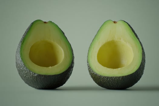 Two halved avocados resting on a subtle green surface in natural light photo