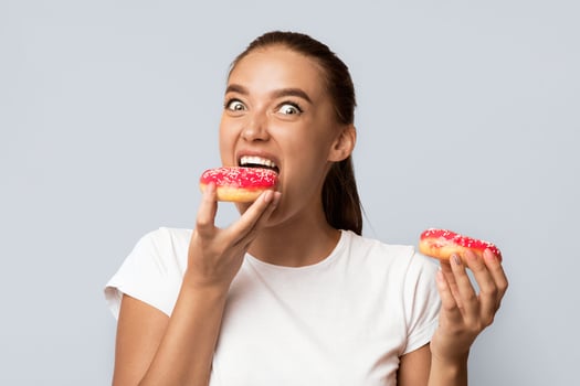 Hungry Girl Eating Donuts Standing Over White Studio Background. Unhealthy Sweets Concept photo