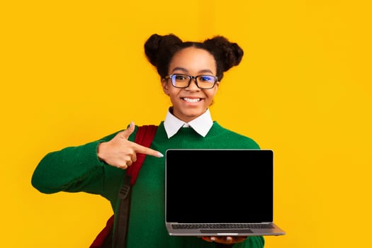 African Schoolgirl Pointing At Laptop Over Yellow Background. Mockup, copy space, panorama photo