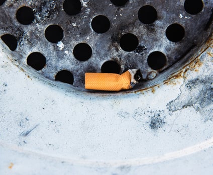 Closeup of a discarded cigarette butt stuck in a rusted metal grate of garbage bin. Nonsmoking, smoking harm, urban pollution, healthy and unhealthy lifestyle, littering, environmental concept. photo