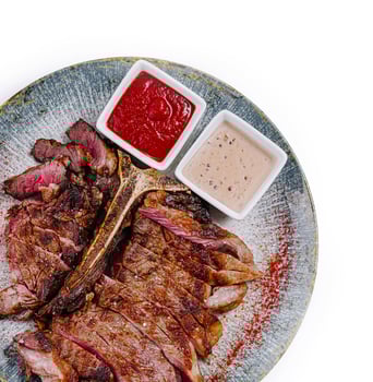 Sliced grilled t-bone steak with sauces on plate, top view photo