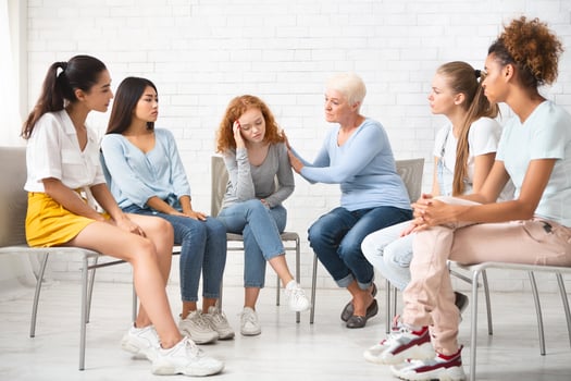 Psychologist Comforting Depressed Girl During Therapy Session With Female Support Group Sitting In Circle Indoors. Selective Focus photo