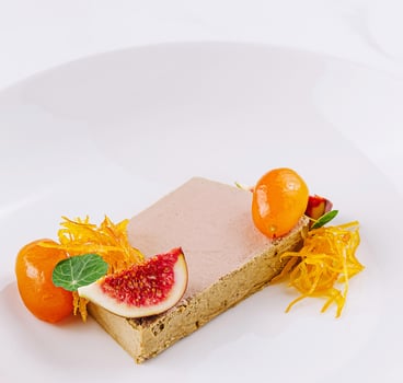 Slice of foie gras served on white plate being garnished with figs and kumquat photo