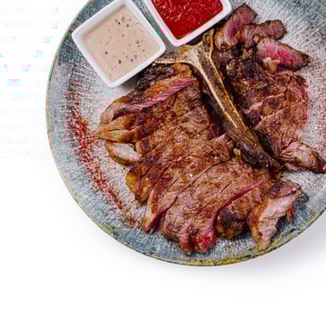 Sliced grilled t-bone steak with sauces on plate, top view photo