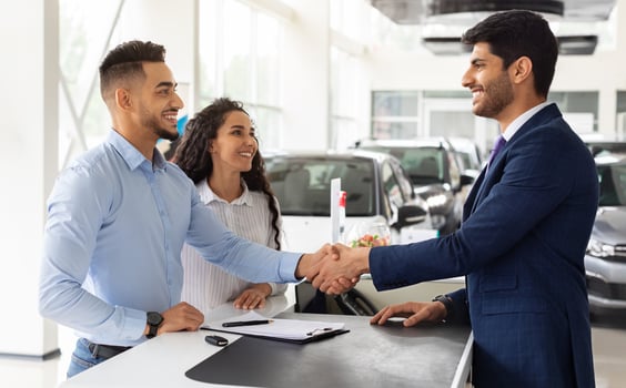 Smiling middle-eastern young man and woman buying car at auto salon, handsome arab guy shaking sales assistant hand, making successful deal, happy family got brand new luxury car, side view photo