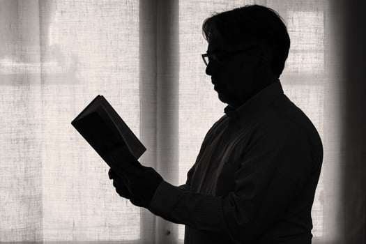 Silhouette of male person reading a book at home near the window. photo