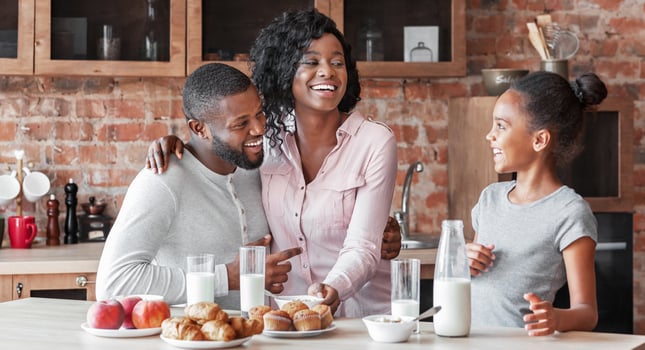 Healthy breakfast together. Cheerful african family drinking milk and eating sweets at kitchen, copy space photo