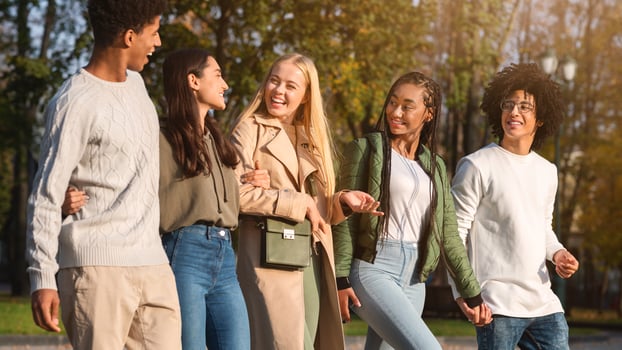Side view of cheerful international friends spending time together outdoors, walking and talking photo
