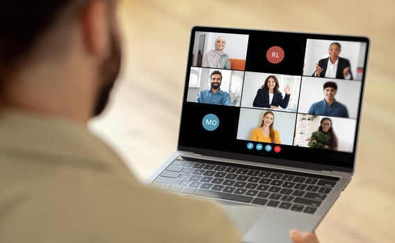 Man using a laptop while a group of people are visible on the screen. The person is engaged in virtual communication or collaboration with the individuals displayed on the laptop screen. photo