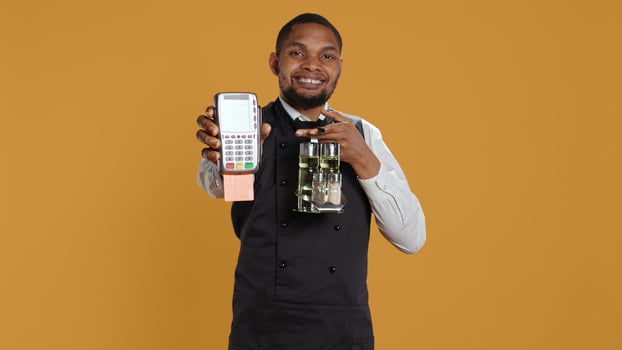 Skilled restaurant employee waiter presenting electronic payment method, showing the pos terminal with a card in it. Confident catering staff working in a customer focused environment. Camera B. photo