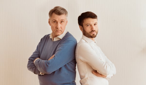 Relationship Problems. Serious Adult Son And Senior Father Standing Back-To-Back Crossing Hands Against White Wall Indoor photo