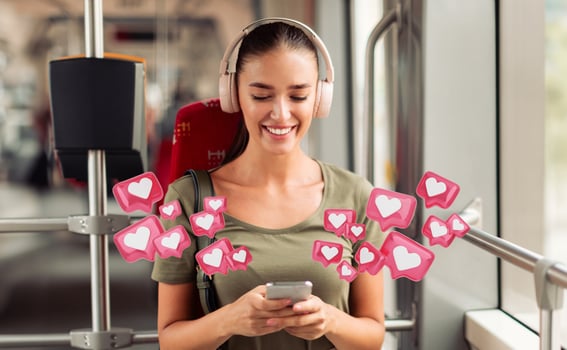 A woman wearing headphones smiles while using her smartphone on a bus or train. The screen is not visible, but she looks pleased as she navigates the digital world photo