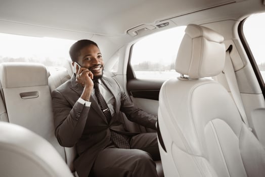Black businessman in a suit is sitting in the back seat of a car while talking on his phone. He has a serious expression on his face and is looking to the side photo