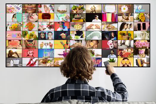 A young person is seated in a living room watching a screen displaying a large grid of colorful images. The images on the screen are diverse, featuring a variety of people, objects, and scenes. photo