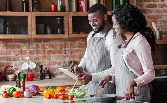Lovely african couple using digital tablet while cooking vegetarian meal, copy space photo