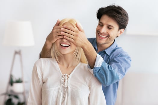 A man surprises his girlfriend with a gift by covering her eyes with his hands. She is smiling in anticipation. photo