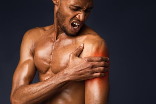 Sports Injury. Shirtless afro man suffering from pain in shoulder, touching hand with red zone, black wall, copyspace photo