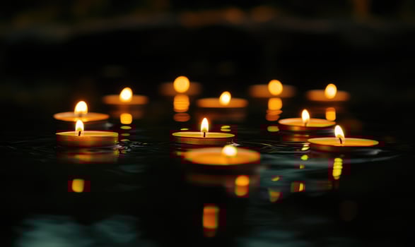 Cluster of small candles floating on rippling water, golden light reflecting softly in the scene photo