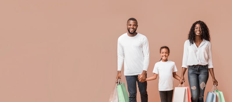 Shopping Weekend. Happy African American family of three walking with shopper bags in studio, yellow background with copy space photo