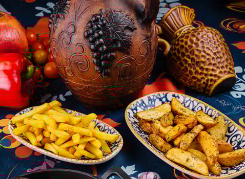 Serving plates overflowing with french fries and potato wedges surrounded by earthenware jugs and fresh vegetables photo