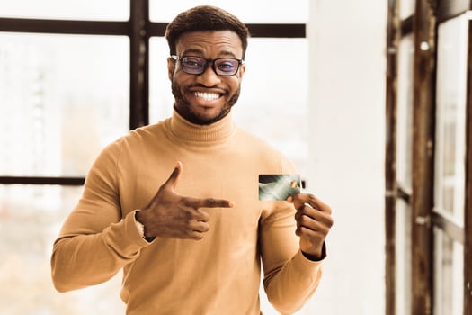 Cashback Concept. Happy black businessman pointing at plastic credit card, recommending it. Copy space photo