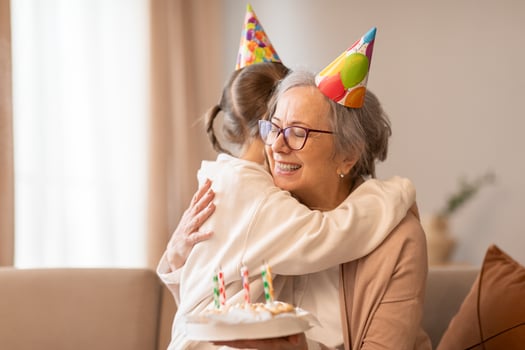 A tender moment captured as an older woman embraces a young girl, both wearing celebratory birthday hats. The affection and joy between them are evident in the heartfelt hug shared. photo