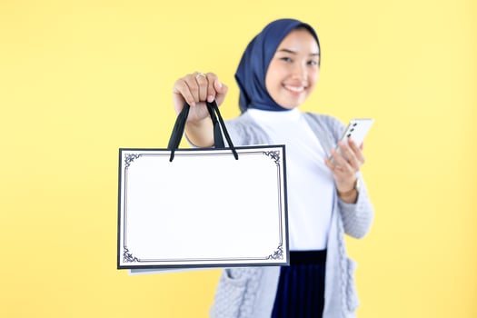 Asian Muslim Woman in Grey Sweater and Hijab Holding Blank Shopping Bag photo