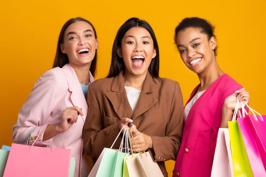 Shopping. Three Joyful Young Ladies With Shopper Bags Smiling To Camera Posing Over Yellow Background. Studio Shot photo