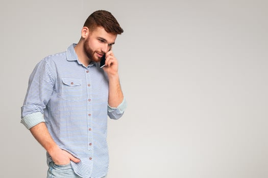 Handsome young bearded man talking on cellphone and looking away on grey studio background, copy space photo