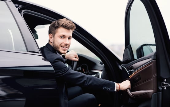 Confident Chauffeur. Guy in suit sitting in driver's seat, getting in his car at downtown area, closing the door photo