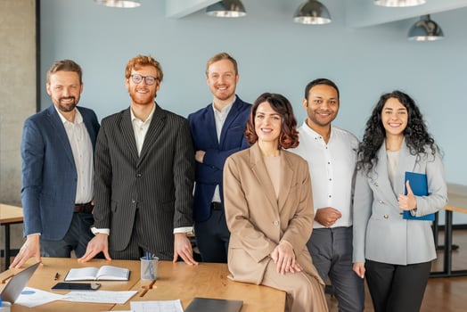 A group of diverse business professionals stand together in a modern office setting. They all look confident and successful, dressed in smart attire, and smiling warmly at the camera photo