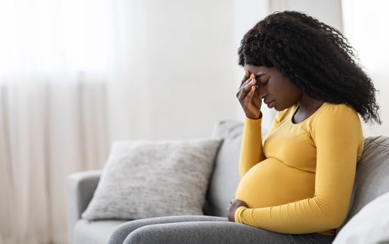 Young pregnant black woman suffering from headache or migraine, feeling sick, sitting on sofa at home, free space. Sad african american expecting lady touching her forehead and big tummy, home alone photo