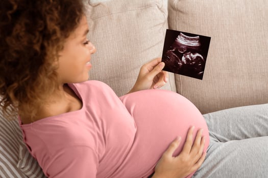 African-american pregnant woman holding ultrasound scan, relaxing on couch photo
