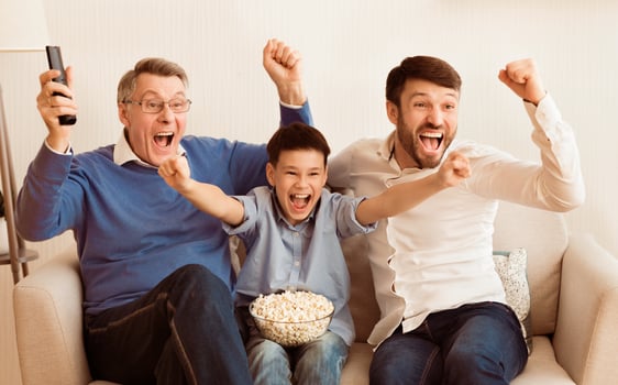 Excited Boy With Father And Grandfather Watching Soccer Match On TV Cheering Favorite Team Sitting On Sofa Indoor. photo