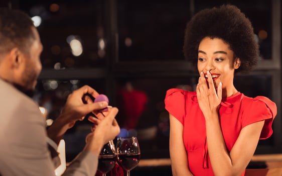 Romantic Proposal Concept. Black Man Proposing To Surprised Woman Offering Engagement Ring, Asking To Marry Him During Date In Restaurant photo