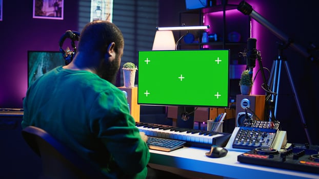 Producer composing music with electronic keyboard notes and green screen display on pc, post production in home studio. Musician artist plays midi controller next to mockup layout. Camera B. photo