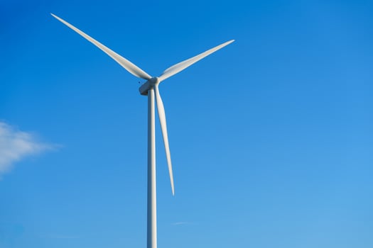 A lone white windmill stands tall against a clear blue sky, symbolizing the beauty of renewable energy. This wind turbine represents an eco-friendly source of power, contributing to a sustainable future. photo