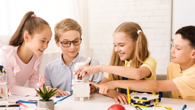 This image shows four children working together on a STEM project in a classroom setting. The children appear to be focused and engaged in their work, and they are all smiling photo