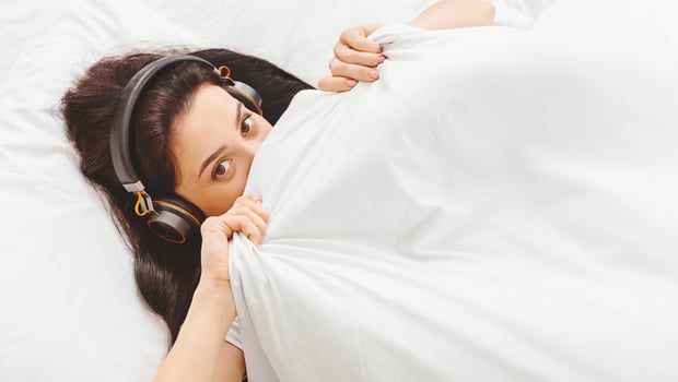 Lady woman is lying in bed early in the morning, listening to music through headphones. She is partially covered by a white blanket, with a relaxed and content expression on her face. photo