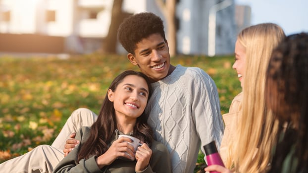 Multiethnic teen couple in love having picnic with friends at public park, copy space photo