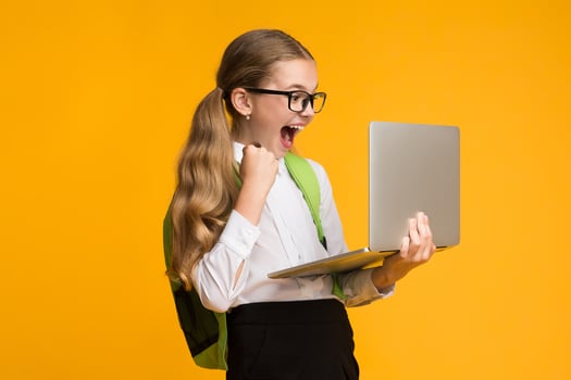 Computer Game Addiction. Overjoyed School Girl Playing Computer Games On Laptop Over Yellow Background In Studio. Free Space For Text photo