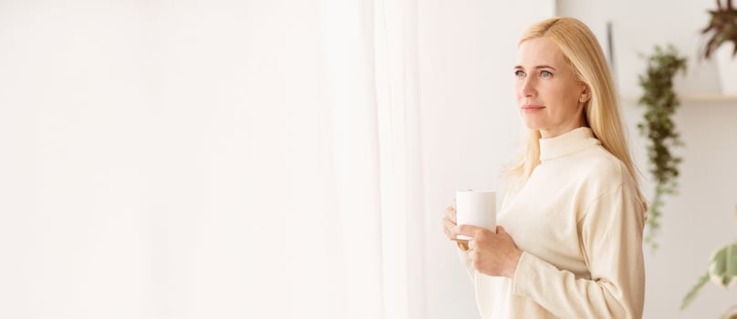 Middle-Aged Woman Drinking Coffee And Looking Through Window, Having Rest At Home photo
