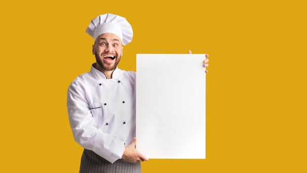 Excited Chef Guy Holding Blank White Poster For Text Recommending Restaurant Menu Standing On Black Studio Background. Mockup photo