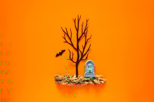 Halloween background with tombstone on dried grass and black tree with a bat on orange background. Minimal concept. photo
