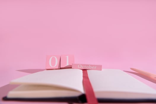 Pink themed calendar displaying the first of October with an open notebook and pencil in a minimalistic setting photo